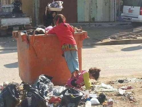 (صورة) مؤثرة.. طفلة ترفع أختها الصغيرة إلى برميل قمامة للبحث عن طعام